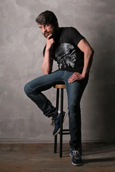 Bearded man sitting on a bar stool and holding his chin. Gray — Stock Photo, Image