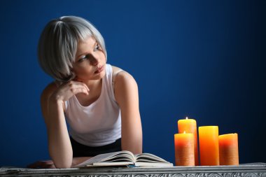 Gümüş peruklu kız kitap ve mumlarla poz verirken. Yakından kapatın. Mavi arka plan