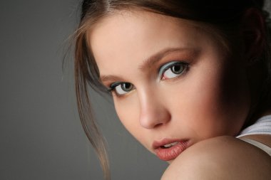 Büyük gözlü bir bayan kameraya bakıyor. Yakından kapatın. Gri arka plan