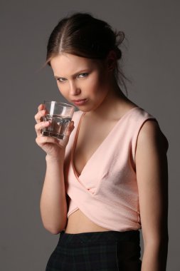 Kız pembe en iyi bardak su ile poz içinde. Yakın çekim. Gri arka planı