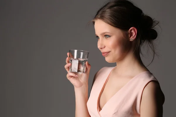 Signora con un bicchiere d'acqua. Chiudete. Fondo grigio — Foto Stock