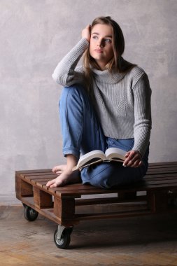 Tahta tahtada kitap olan bir kız. Gri arka plan
