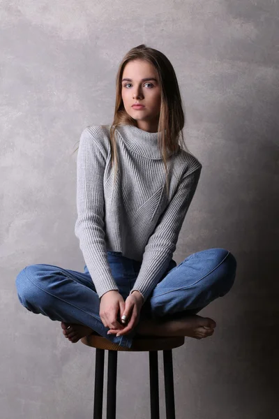 Menina em uma cadeira de bar com pernas cruzadas. Fundo cinzento — Fotografia de Stock