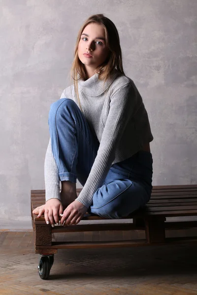 Sitzendes Mädchen, das auf einem Deck posiert. grauer Hintergrund — Stockfoto