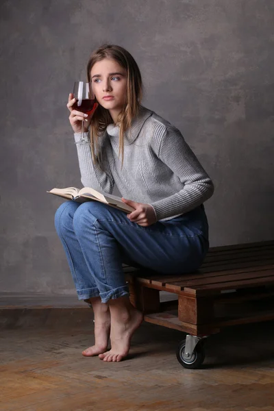 Siedząc dziewczynę z książką i kieliszek wina. Szare tło — Zdjęcie stockowe