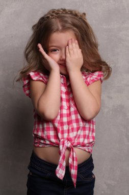 Küçük sarışın elleriyle gözlerini kapatıyor. Yakından kapatın. Gri arka plan