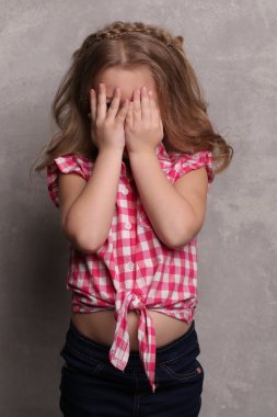 Bebek elleriyle gözlerini kapatıyor. Yakından kapatın. Gri arka plan