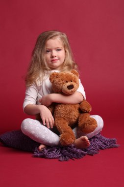 Pijamalı çocuk bir ayıya sarılıyor. Kırmızı arka plan