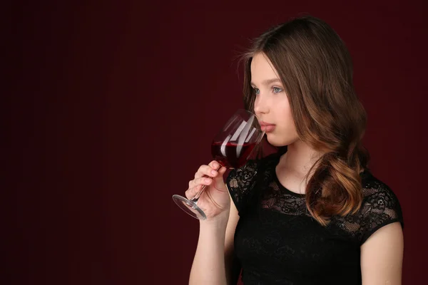 Ragazza che tocca il bicchiere da vino con le labbra. Chiudete. sfondo rosso scuro — Foto Stock