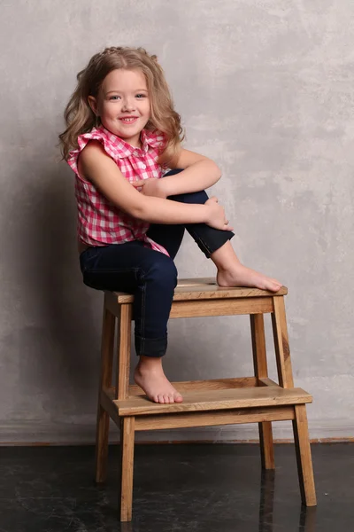 Portret van een klein meisje met make-up poseren op stoel. Grijze achtergrond — Stockfoto