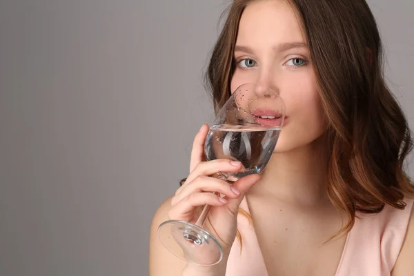 Ragazza che beve acqua da un bicchiere di vino. Chiudete. Fondo grigio — Foto Stock
