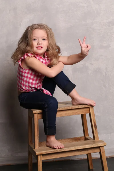 Menina de camisa xadrez posando em uma cadeira. Fundo cinzento — Fotografia de Stock