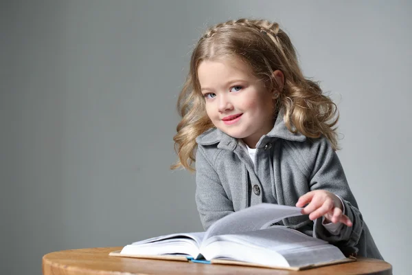 Portret van baby meisje in vacht met een boek. Close-up. Grijze achtergrond — Stockfoto