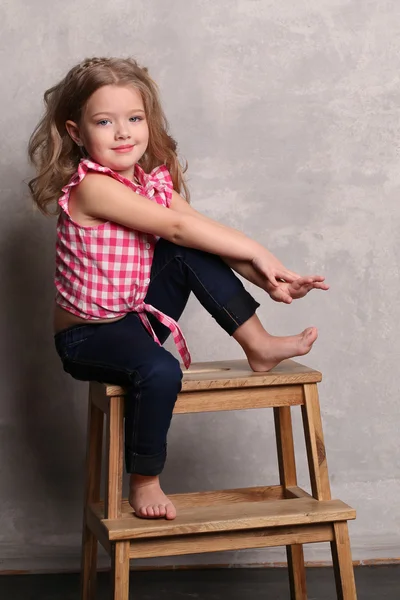 Kid i pläd skjorta poserar på en stol. Grå bakgrund — Stockfoto