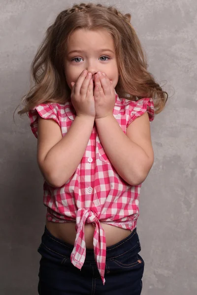 Barnflicka som stänger munnen med händerna. Närbild. Grå bakgrund — Stockfoto