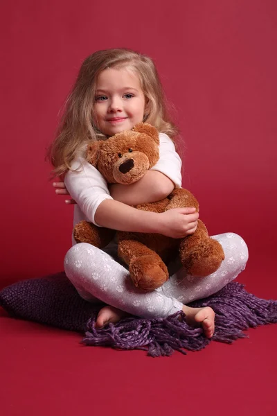 Baby in pyjama knuffelen een beer. Rode achtergrond — Stockfoto