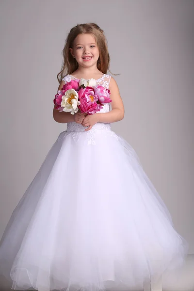 Petite fille en robe de mariée avec plein de fleurs. Fond gris — Photo