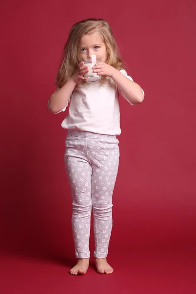 Flicka i pyjamas dricker mjölk. Röd bakgrund — Stockfoto