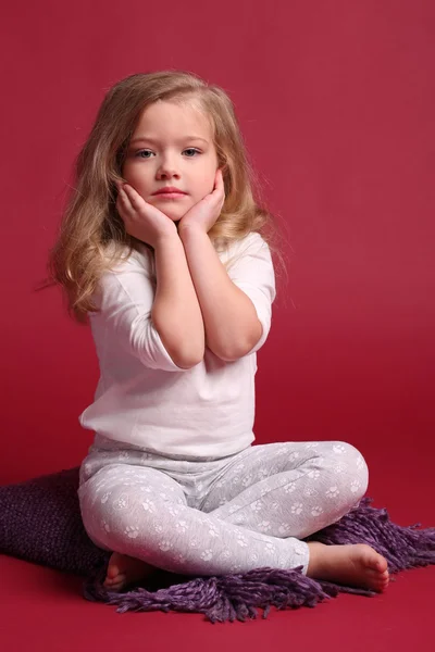 Bebê de pijama tocando suas bochechas. Fundo vermelho — Fotografia de Stock