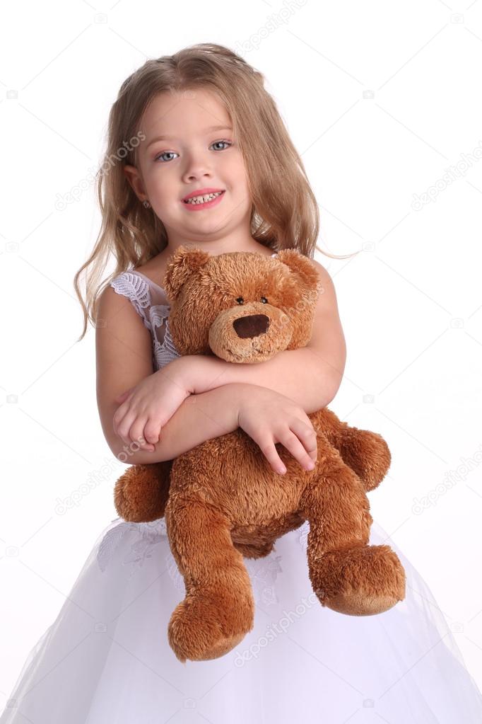 Little girl in wedding dress with bear. Close up. White background