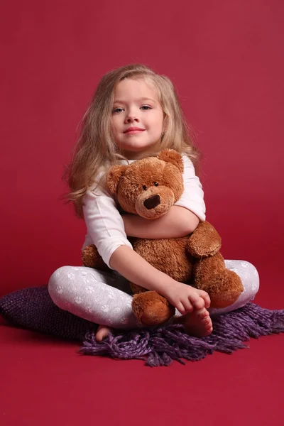 잠옷을 입은 아이가 곰을 껴안고 있습니다. 빨간색 배경 — 스톡 사진