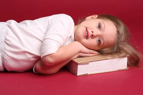 Niño en ropa de dormir acostado en un libro. De cerca. Fondo rojo —  Fotos de Stock