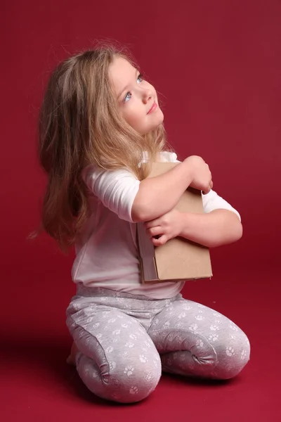 Sitting girl in pajamas hugging a book. Red background