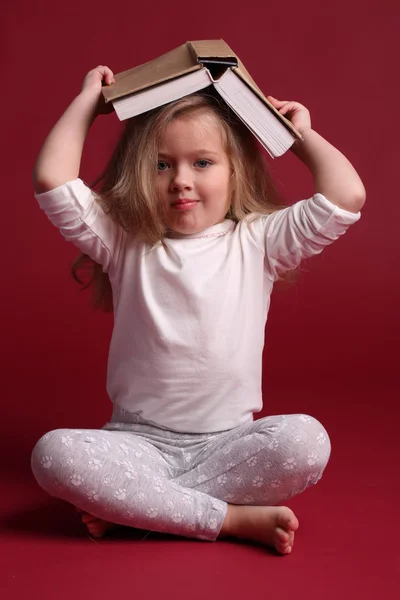 Dziecko w piżamie z książką na głowie. Czerwone tło — Zdjęcie stockowe