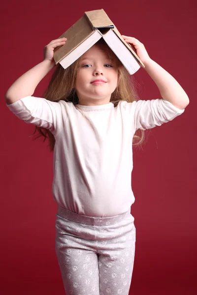 Dzieciak w piżamie z książką na głowie. Z bliska. Czerwone tło — Zdjęcie stockowe