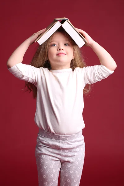 Bebé en pijama con un libro en la cabeza. De cerca. Fondo rojo —  Fotos de Stock