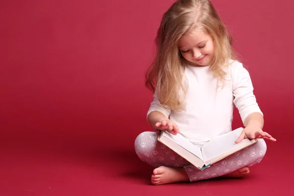 Niño en pijama leyendo un libro. Fondo rojo —  Fotos de Stock
