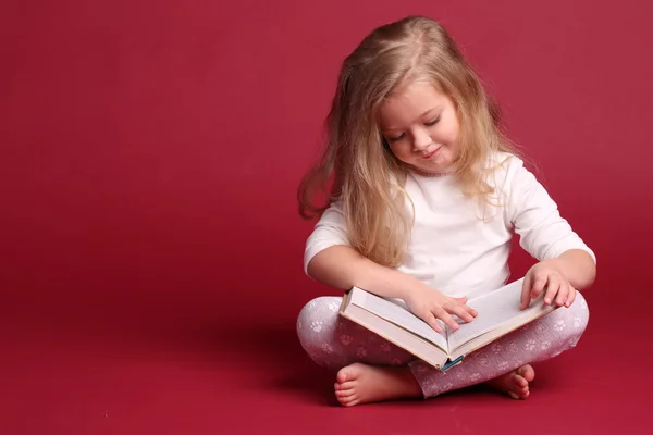 Bebé en pijama leyendo un libro. Fondo rojo —  Fotos de Stock