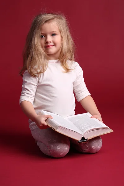 Siedząc dziecko w bieliznę nocna z książką. Czerwone tło — Zdjęcie stockowe