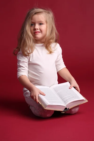 Сидяча дівчина в сплячому одязі з книгою. Червоний фон — стокове фото