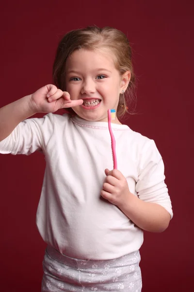 Baby with toothbrush touching her teeth. Close up. Red background — Stock Photo, Image