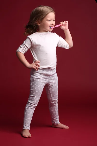 Baby Girl borsta tänderna och poserar. Röd bakgrund — Stockfoto