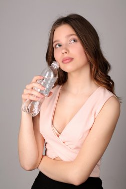 Bir şişe su yla düşünen bir kız. Yakından kapatın. Gri arka plan