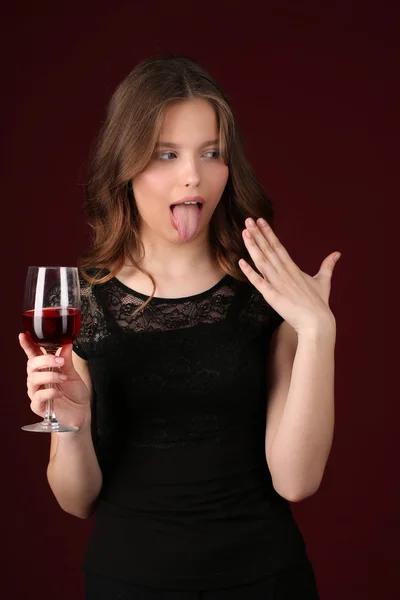 Ragazza con bicchiere da vino che mostra la lingua. Chiudete. sfondo rosso scuro — Foto Stock