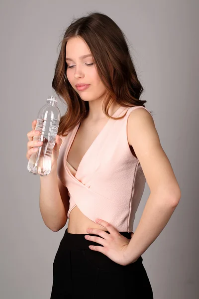 Mädchen mit Blick auf die Wasserflasche. Nahaufnahme. grauer Hintergrund — Stockfoto