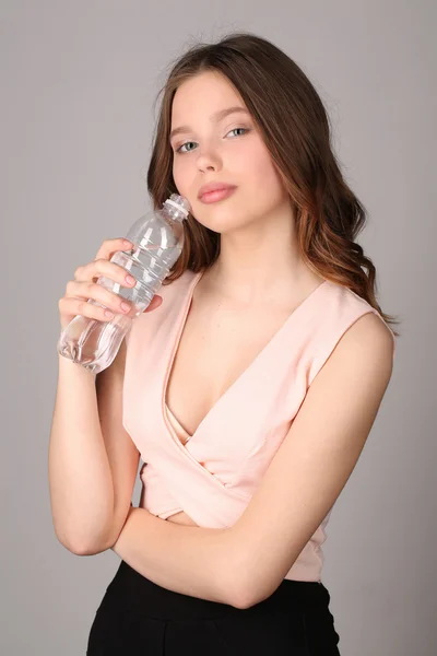 Mädchen berührt ihr Gesicht mit einer Wasserflasche. Nahaufnahme. grauer Hintergrund — Stockfoto