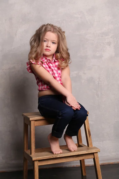 Baby flicka sitter på en stol. Grå bakgrund — Stockfoto