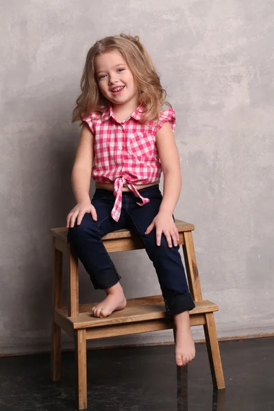 Flicka i pläd skjorta poserar på en stol. Grå bakgrund — Stockfoto