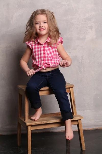 Niña con camisa a cuadros posando en una silla. Fondo gris —  Fotos de Stock