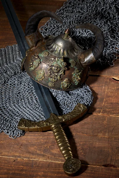 Меч и солдатский шлем с рогами на деревянном фоне — стоковое фото