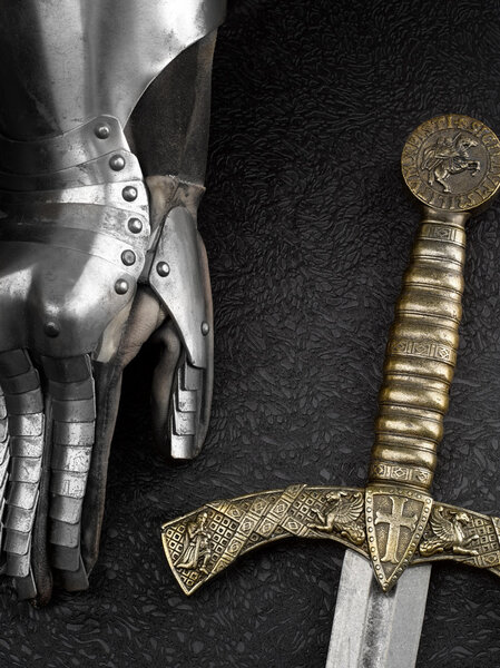 The iron glove of a knight and a sword on a beautiful dark background.Studio high-resolution image.