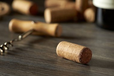 Bir şişe şarabın mantarının yakın çekimi ahşap bir masanın üzerinde, diğer mantarların arka planına ve bir şişe kırmızı şaraba dayanır..