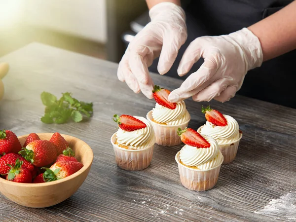 Close-up of a pastry chef decorating cooked muffins with fresh strawberries.