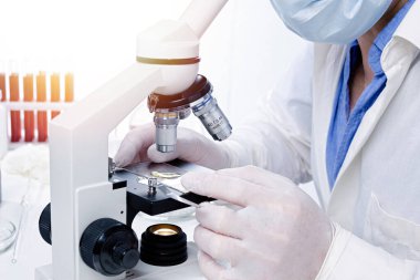 Bilimadamı veya laboratuvar asistanı, laboratuvar tıbbi ekipmanlarının arka planına karşı bir mikroskop ile araştırma yapar..