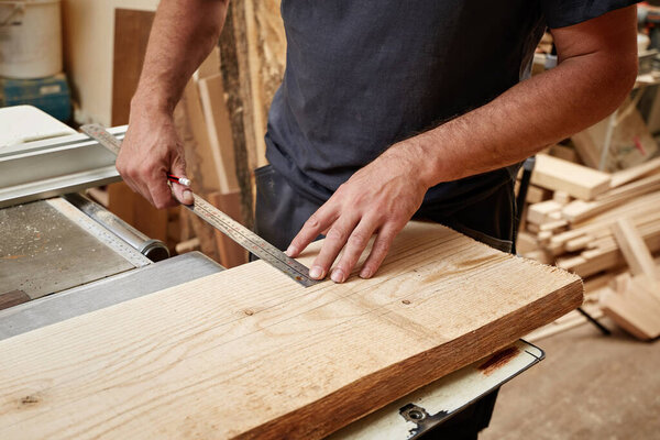 The carpenter takes measurements on a wooden board for further sawing with a circular saw.