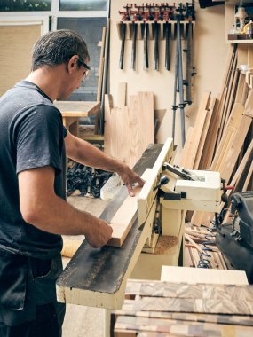 Jointer üzerinde çalışan bir marangozun yakın çekimi. Atölyesinin arka planında.